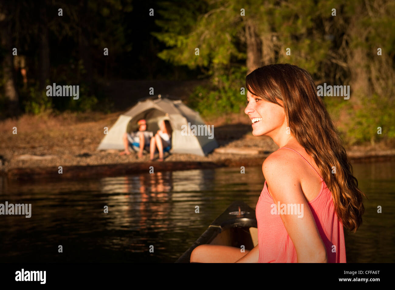 Une jeune femme sourit tout en canoë sur un voyage de camping au bord d'un lac dans l'Idaho. Banque D'Images