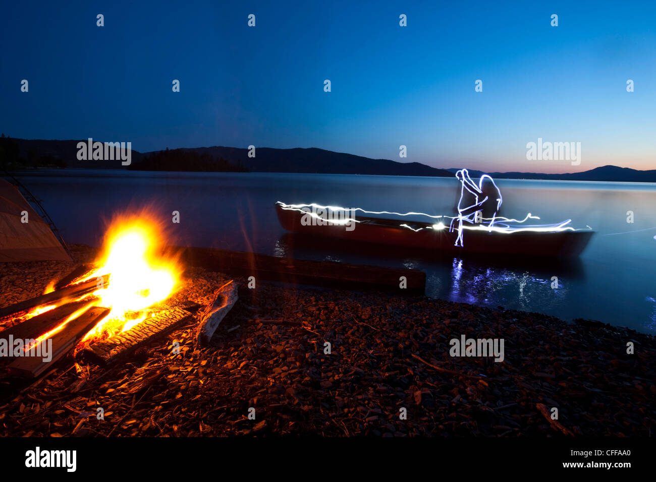 Peinture lumière décrit un homme canoë par un feu de camp de la rive d'un lac de l'Idaho. Banque D'Images