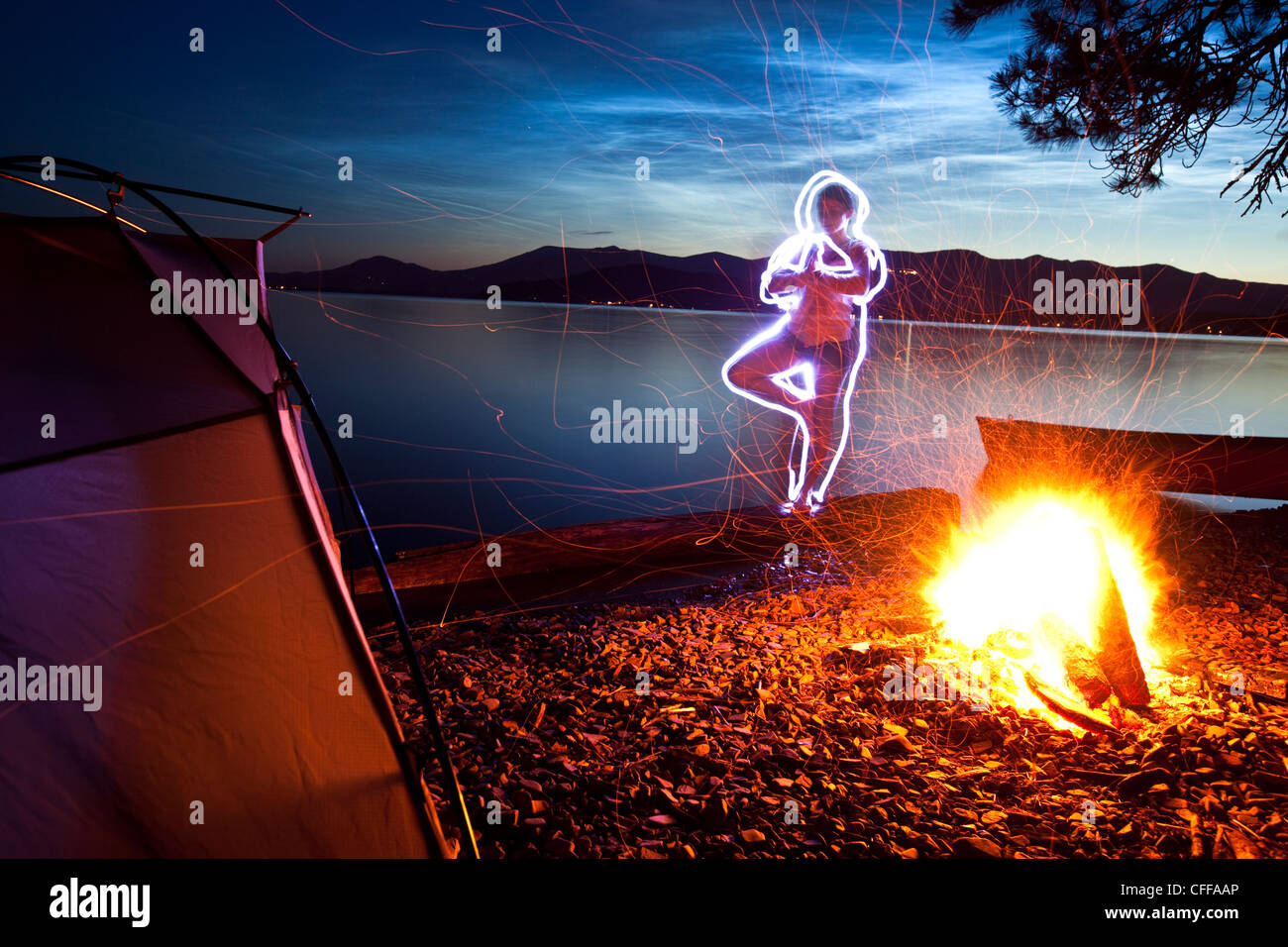 Une peinture d'un couple à côté de sa tente et feu de camp sur un voyage de camping le long des rives d'un lac, dans l'Idaho. Banque D'Images