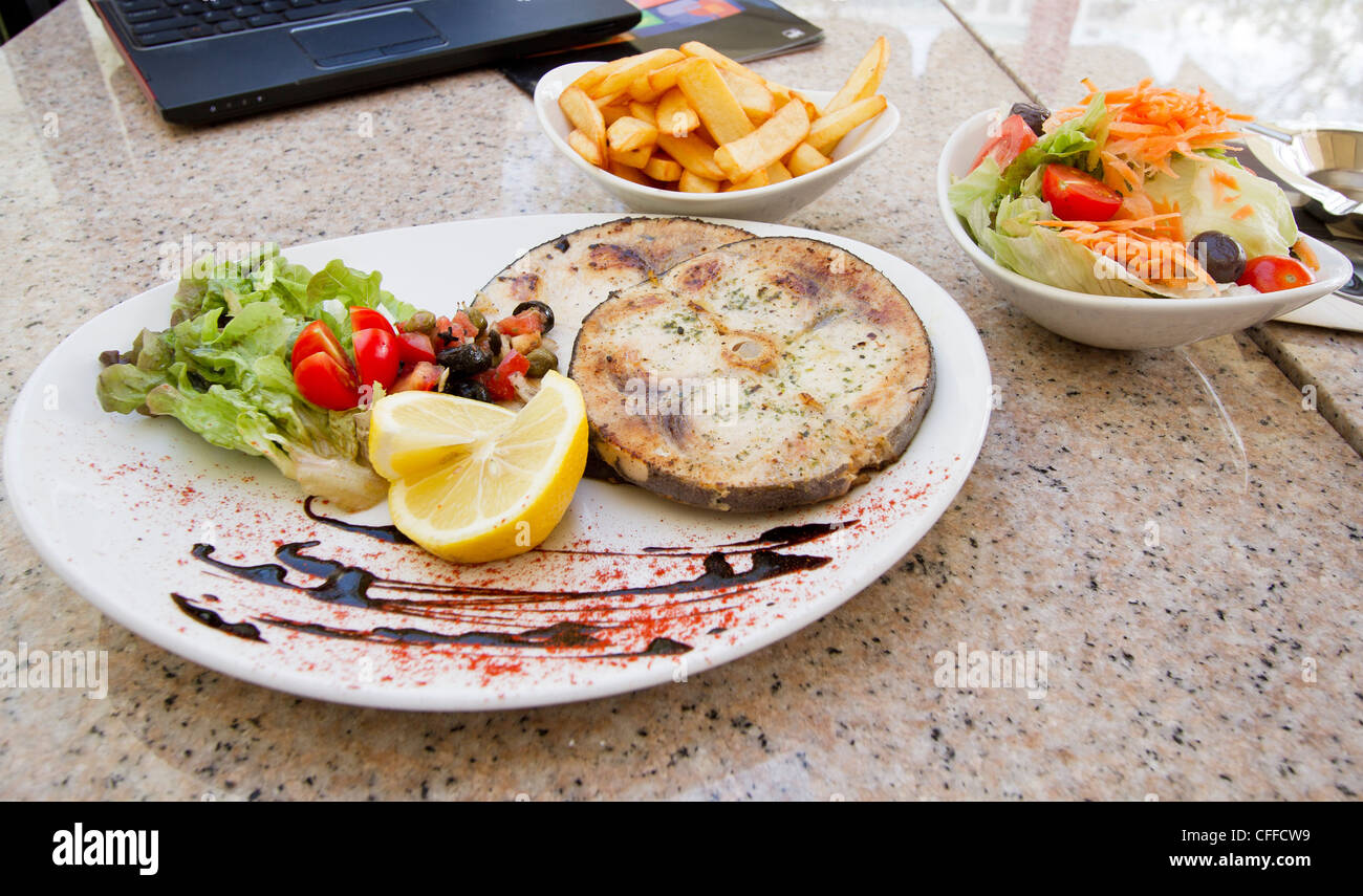 Steak d'espadon servi sur la plaque avec du citron et des légumes et pommes frites et salade sur le côté Banque D'Images