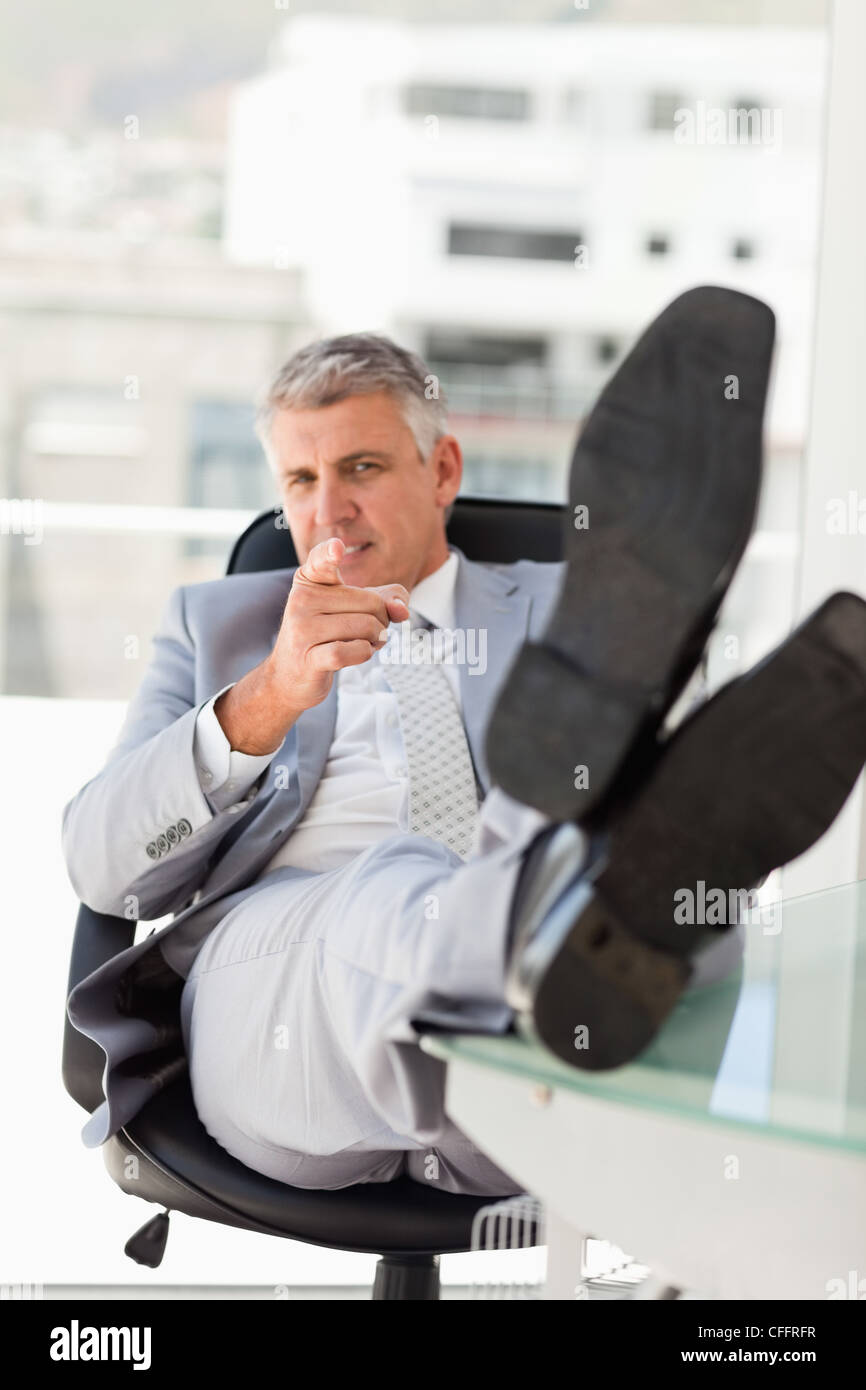 Portrait d'un patron avec les pieds sur son bureau tout en indiquant