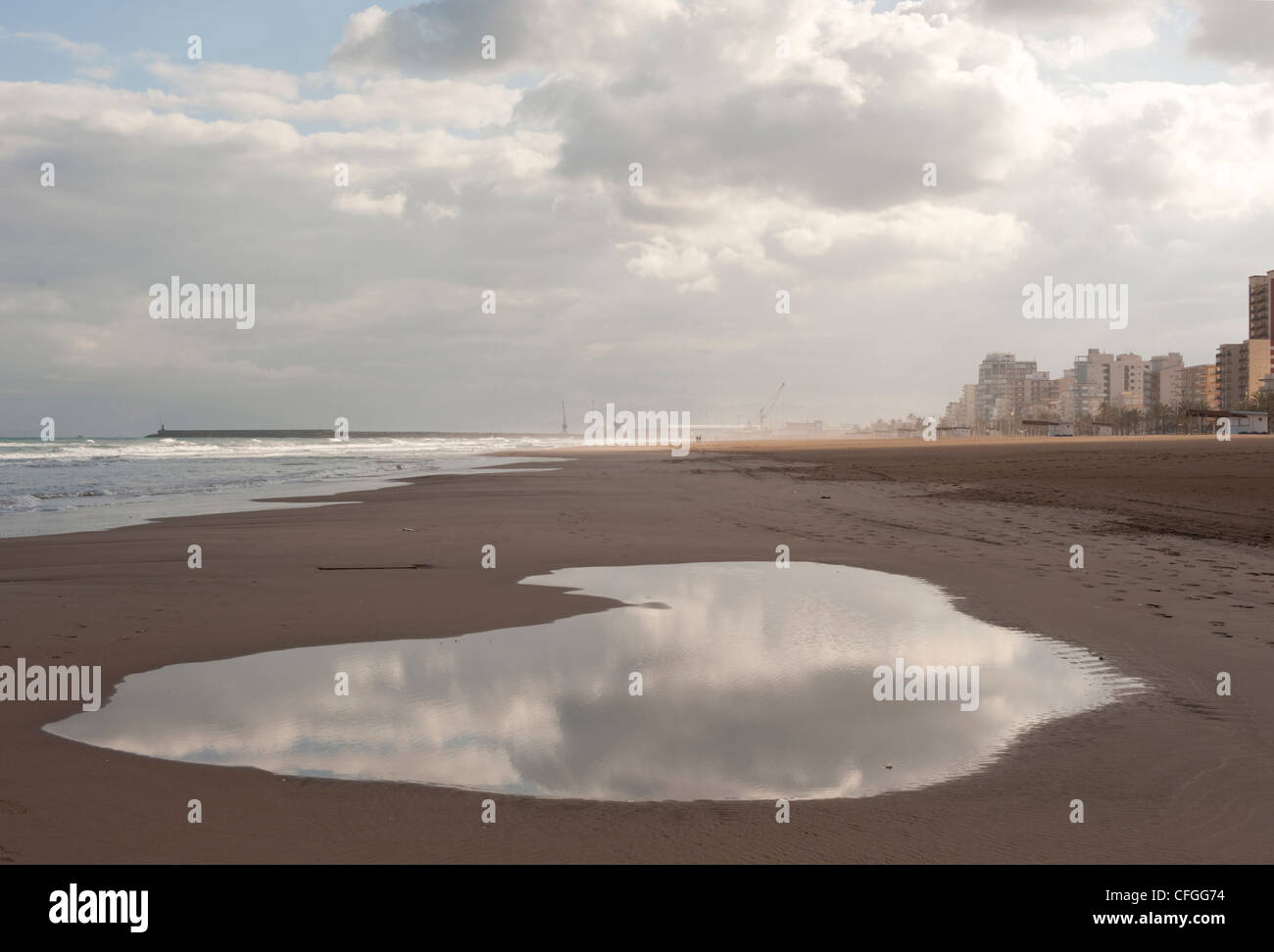 Une grande flaque reflète un ciel nuageux orageux au-dessus de la mer que la pluie s'installe en hiver sur la station balnéaire de Gandia, Espagne Banque D'Images