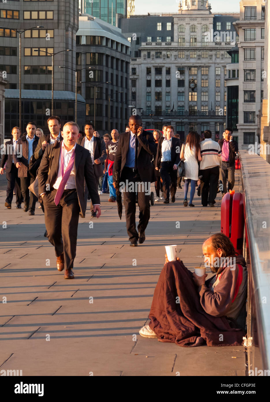 Les banlieusards de marcher à travers le pont de Londres dans le quartier financier de la ville de London England UK avec des sans-abri en premier plan Banque D'Images
