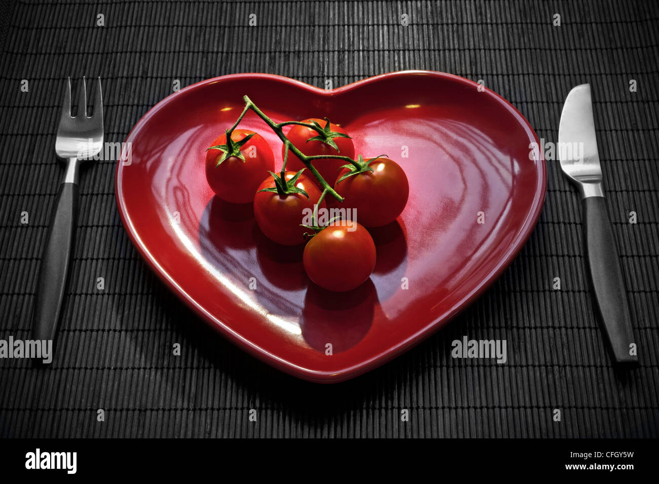 Les tomates sur la plaque en forme de coeur rouge, avec la table, manger frais et sain régime. Banque D'Images