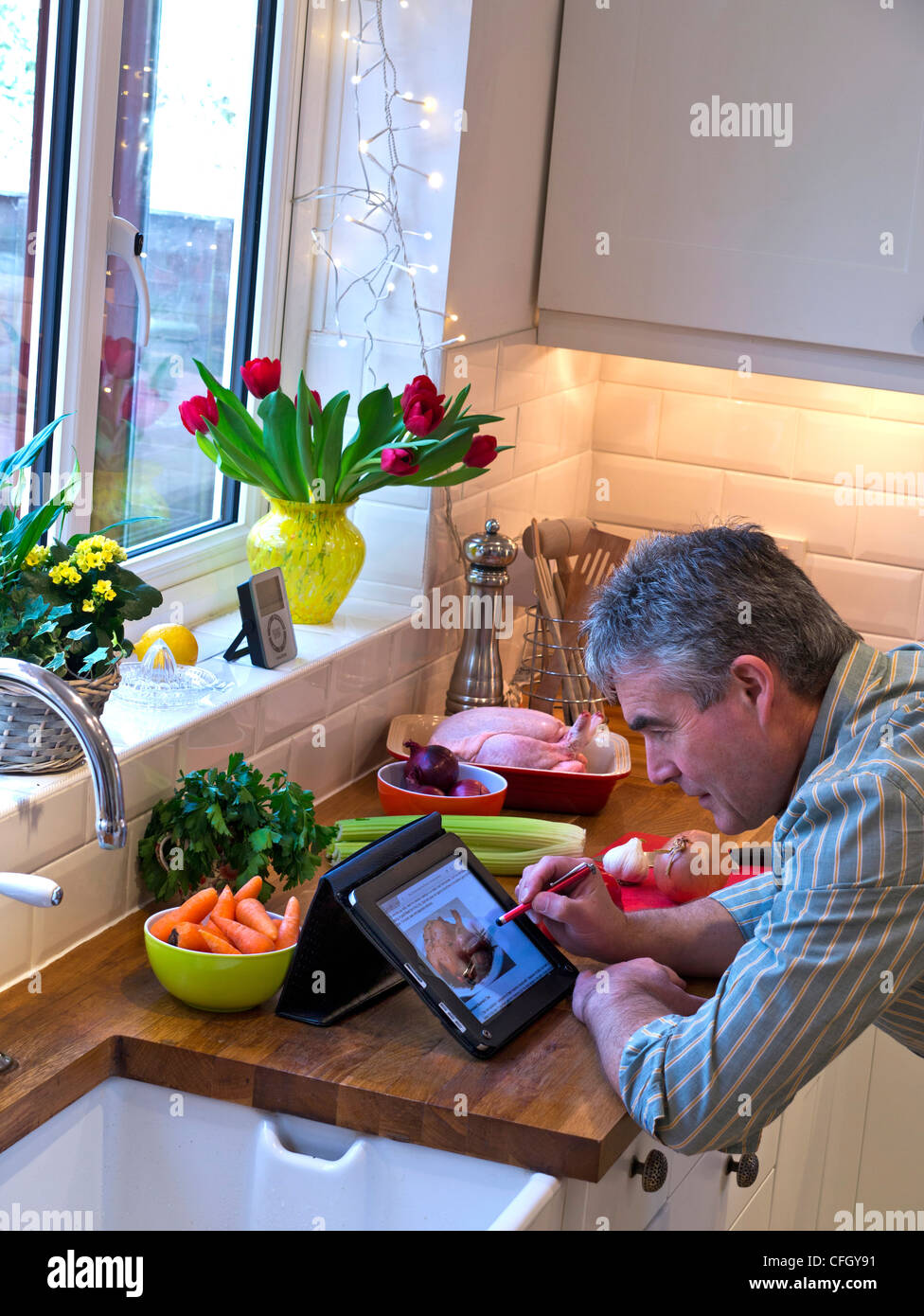 La préparation de repas de poulet rôti l'homme contemporain à l'aide de cuisine à domicile ordinateur tablette iPad pour fournir une recette en ligne Banque D'Images