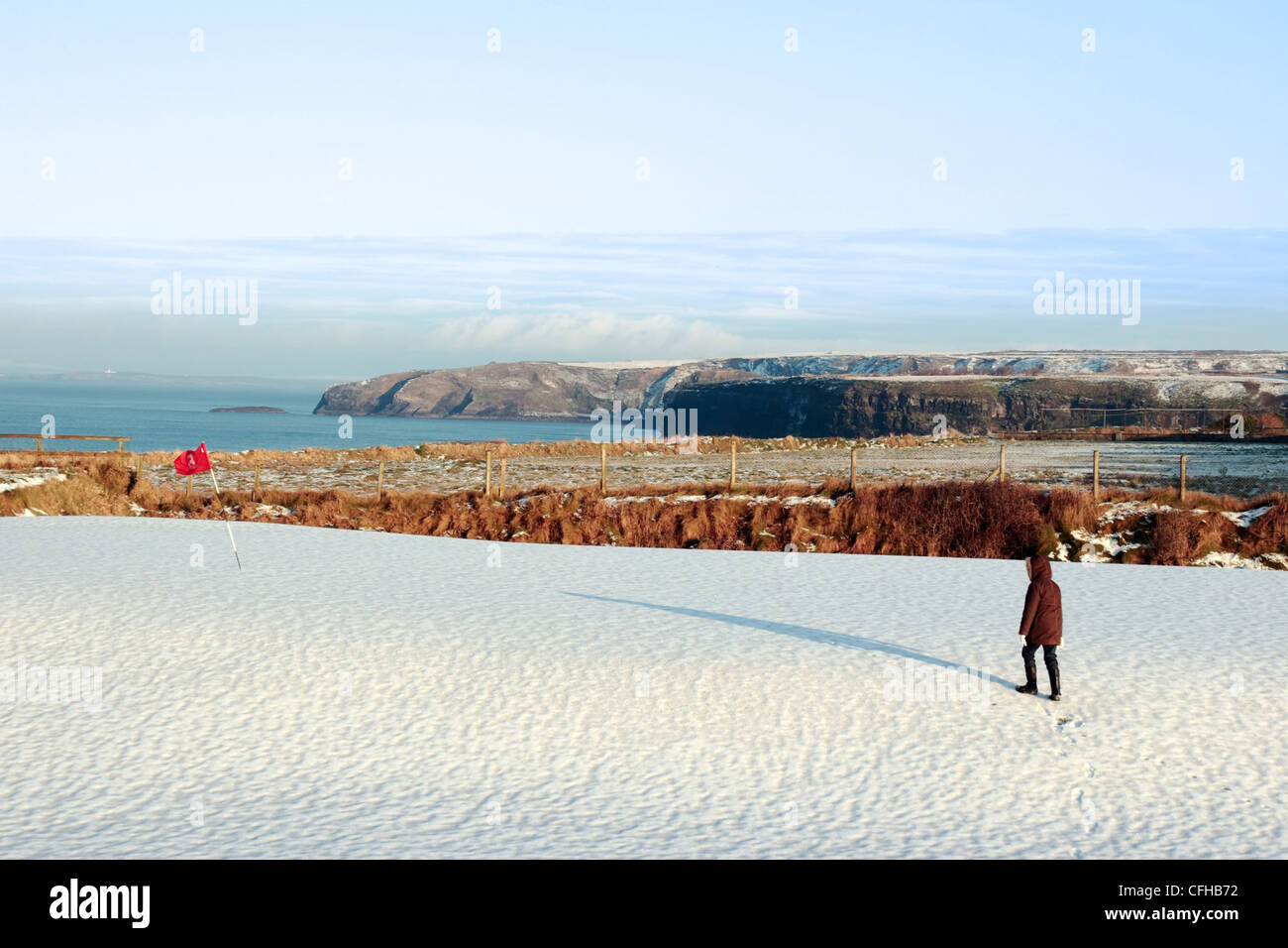 Enfant sur un couvert de neige golf en Irlande en hiver avec vue sur la mer et les falaises en arrière-plan Banque D'Images