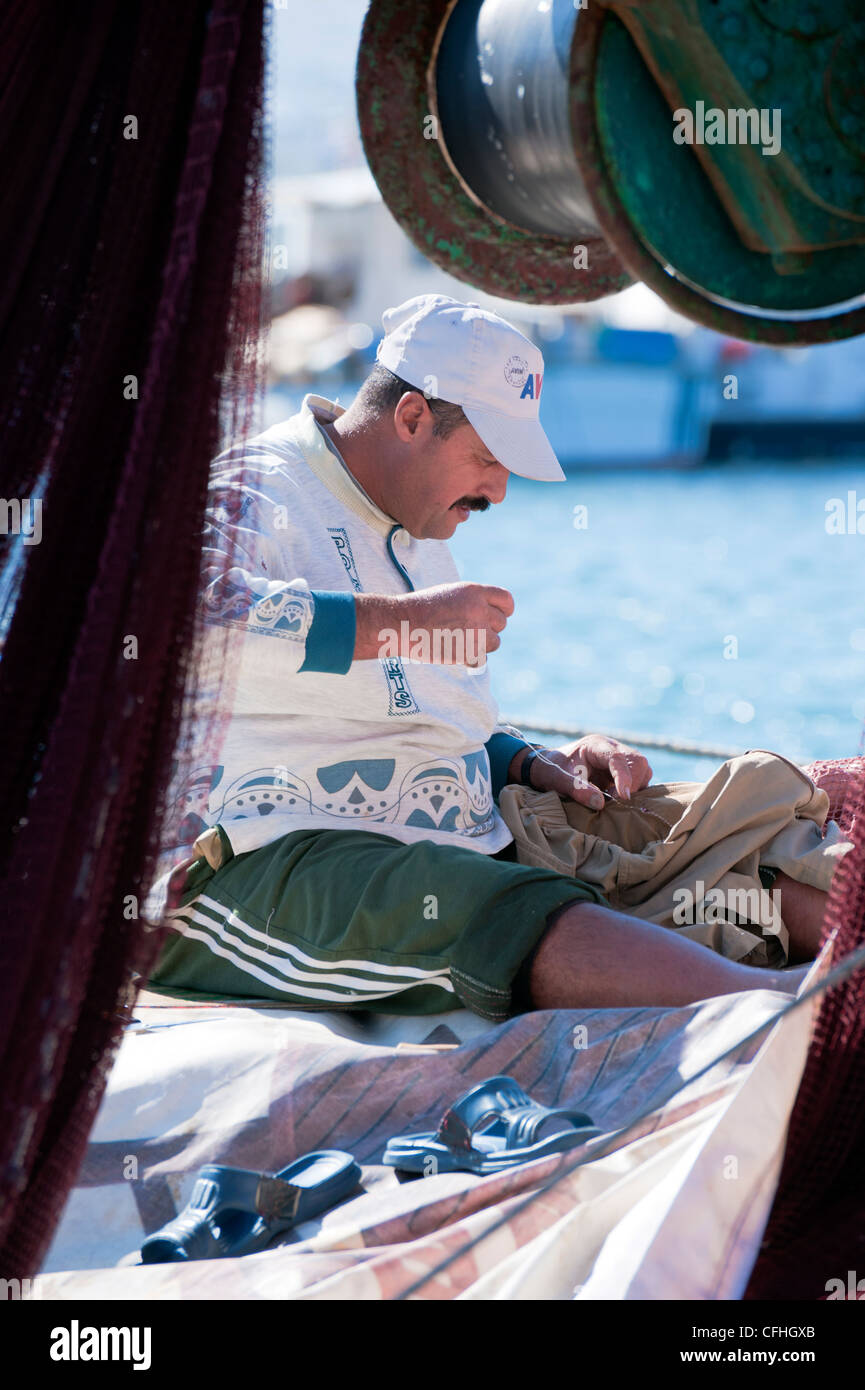 Pêcheur grec la couture d'un vêtement dans le port de Naoussa, sur l'île de Paros Cyclades grecques. Banque D'Images