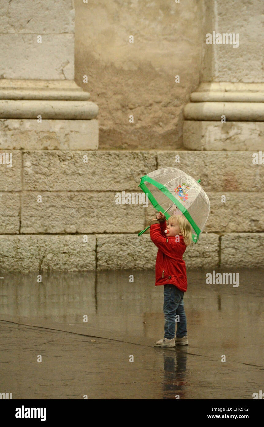 Fille dans la pluie avec parapluie et sucette dans Arco, Italie. Banque D'Images