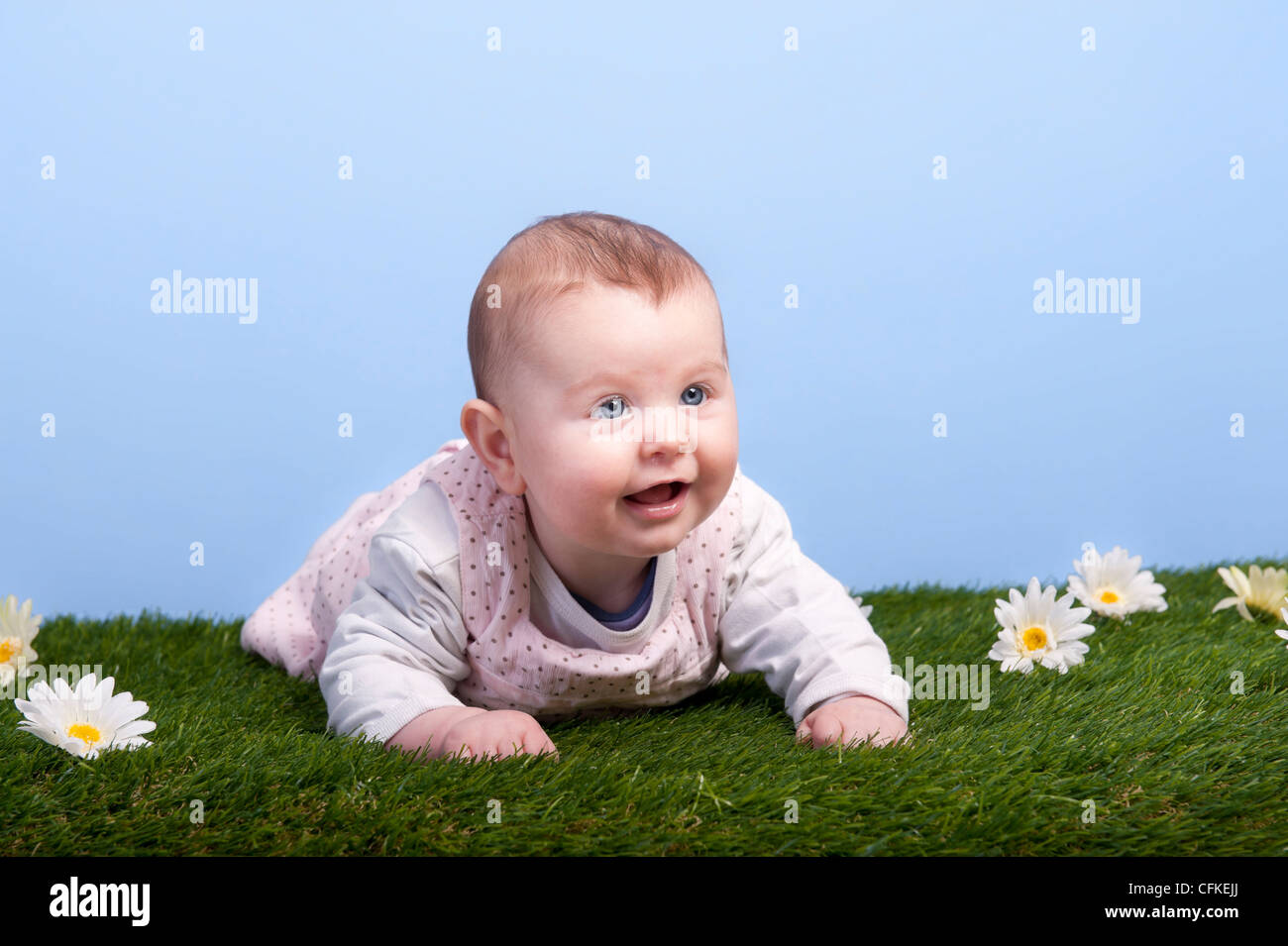 Baby lying on grass against a blue sky Banque D'Images