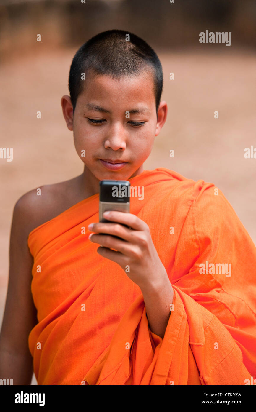 Moine Bouddhiste novice en robe safran d'un village près du fleuve Mékong, le Laos avec téléphone mobile Banque D'Images