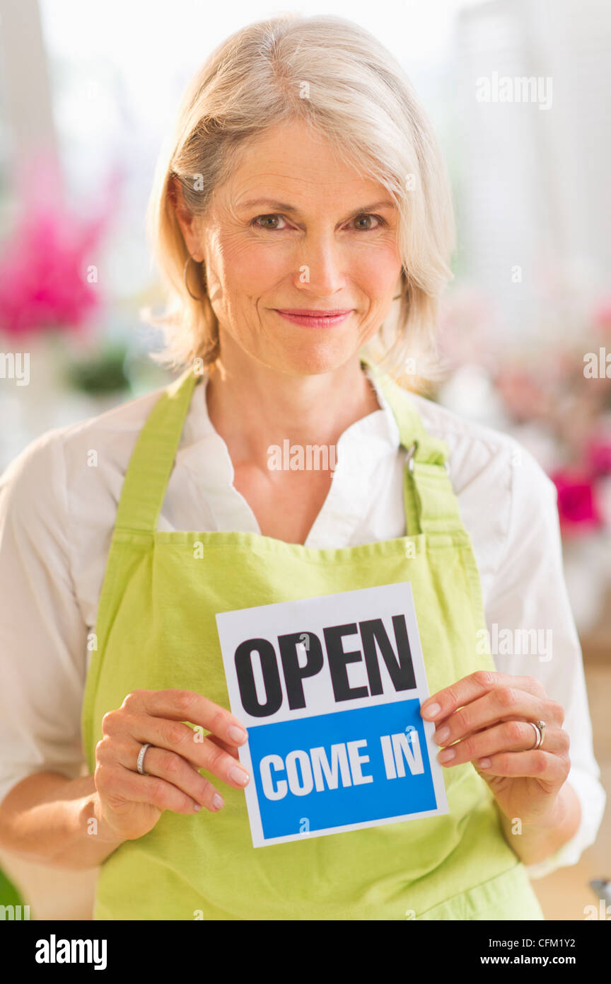 USA, New Jersey, Jersey City, Portrait of senior female florist montrant open sign and smiling Banque D'Images