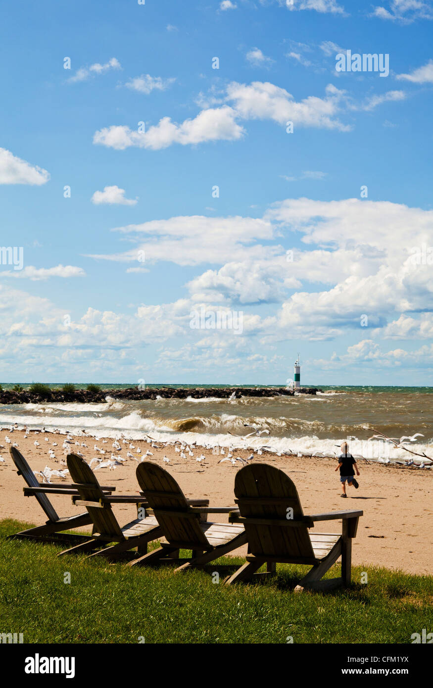 Chaises adirondack sur le lac Érié plage avec petit garçon courir après les mouettes sous un ciel bleu lumineux, puffy nuage blanc, le phare Banque D'Images