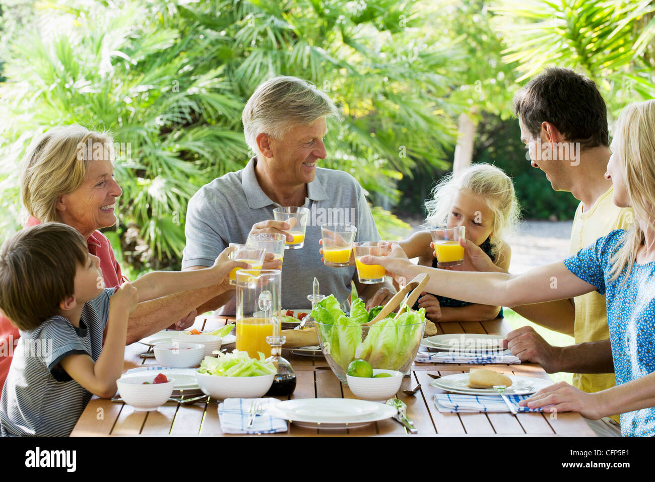 Multi-generation family toasting with orange juice outdoors, portrait Banque D'Images