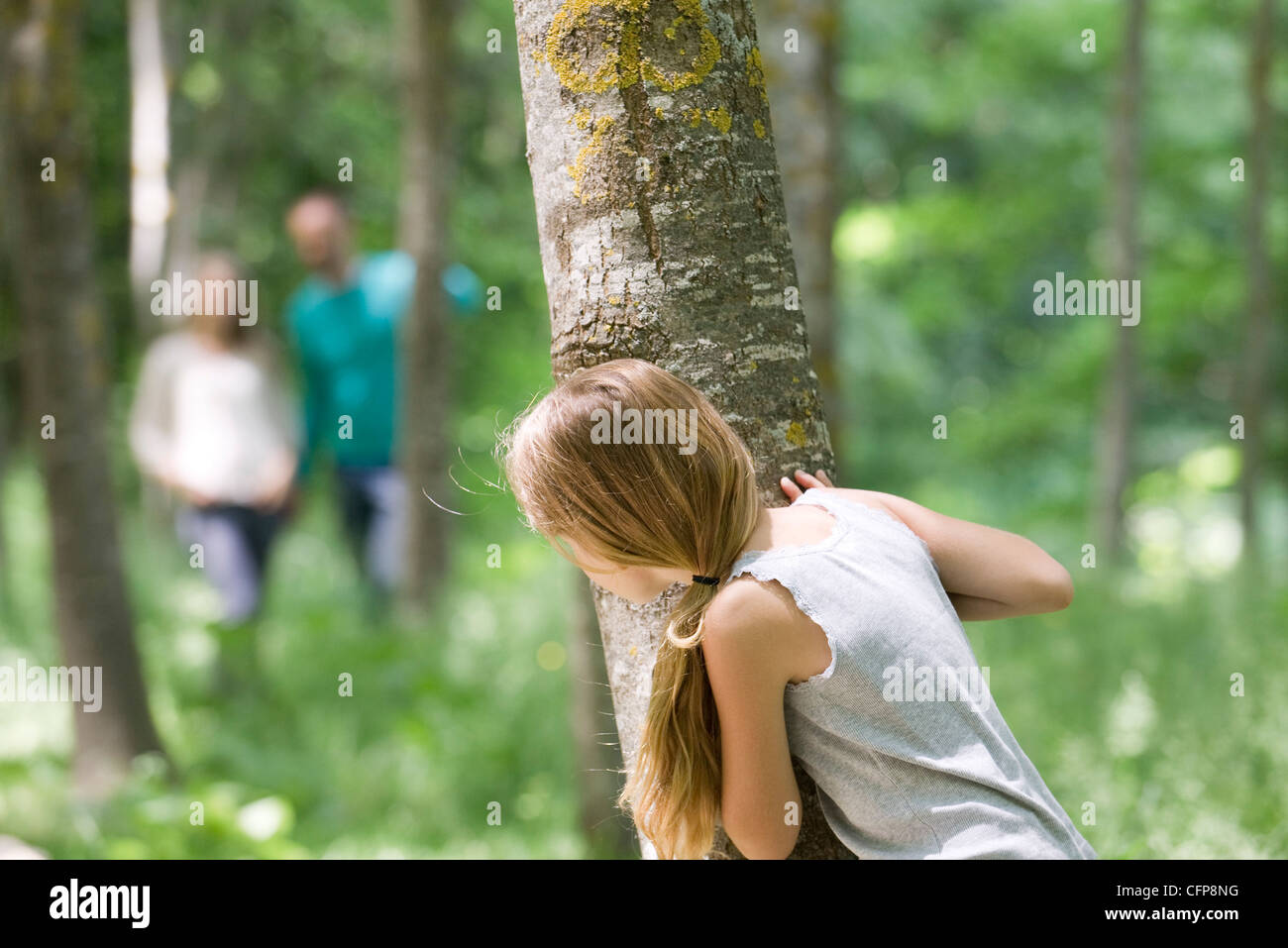 Girl hiking derrière tree in woods Banque D'Images