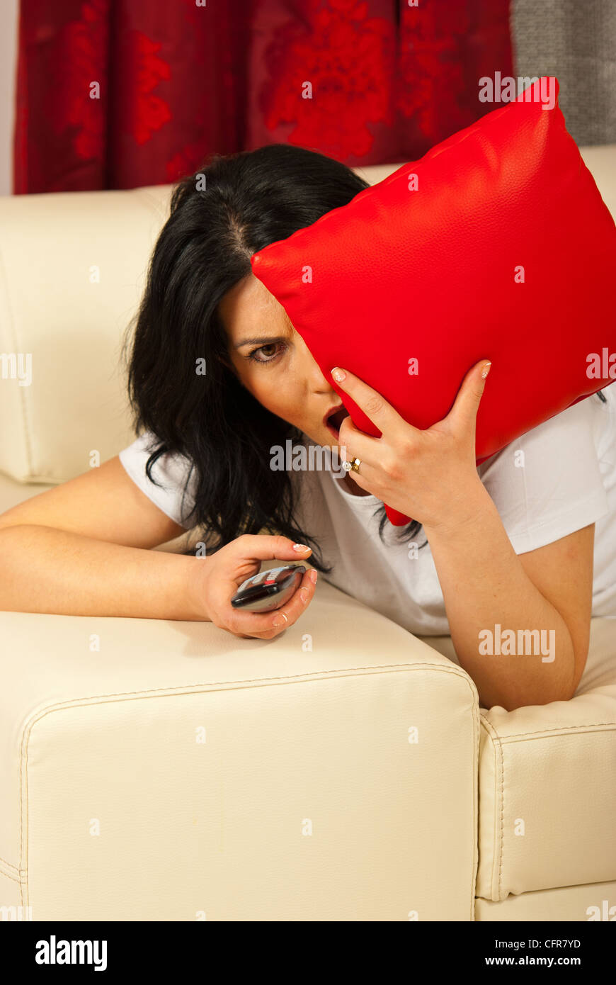 Femme seule portant sur canapé devant un film d'horreur à la télévision et d'être effrayé et couvrant eye avec oreiller Banque D'Images