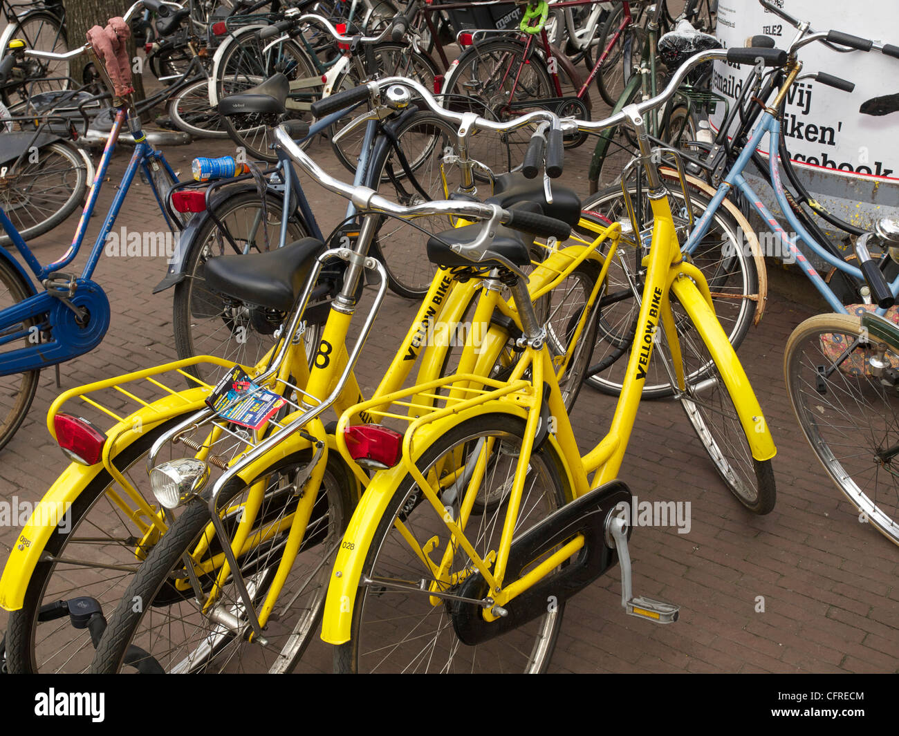 Service de location de vélos jaune garée dans une mer de vélos sur le trottoir à Amsterdam Banque D'Images