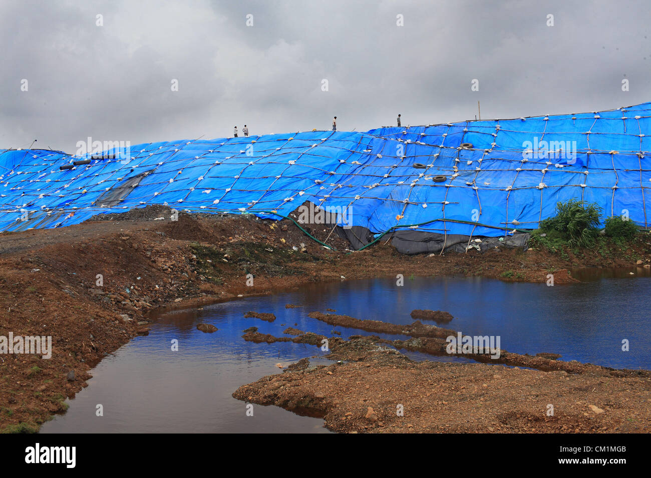 11 septembre 2012 - Ahmedabad, Gujarat, Inde - les travailleurs d'une décharge de déchets solides au centre de développement industriel Gujarat Silvassa pour effacer les déchets toxiques qui avait renversé à la proximité des terres agricoles. L'ensemble de la zone a été couverte de feuilles de couverture de pluie afin d'empêcher l'inondation du site des déchets avec de l'eau de pluie de mousson et causer davantage de dommages.Le site d'élimination des déchets contient beaucoup de déchets toxiques et dangereux de l'industrie chimique située à Ahmedabad. Le Blacksmith Institute, qui surveille les pires endroits de la terre polluée s'est souvent classé dans le top 10 Silvassa pire po Banque D'Images