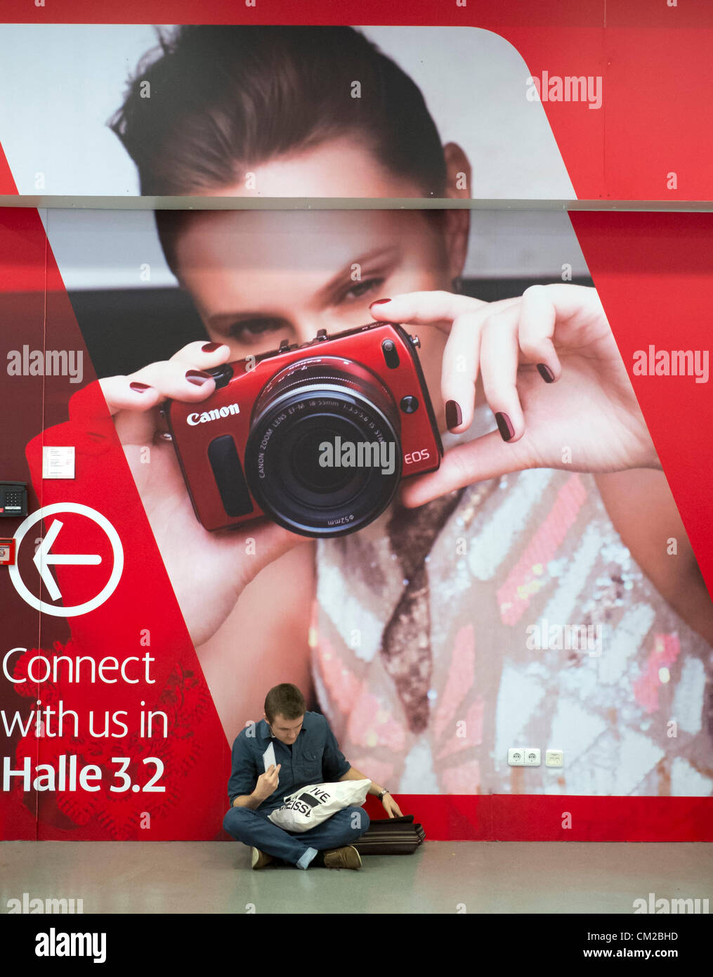 Visiteur assis devant la grande affiche publicité nouveau appareil photo Canon sur deuxième journée bi-annuelle de la photographie et imagerie Photokina salon de Cologne en Allemagne ; le mercredi 19 septembre 2012. Banque D'Images