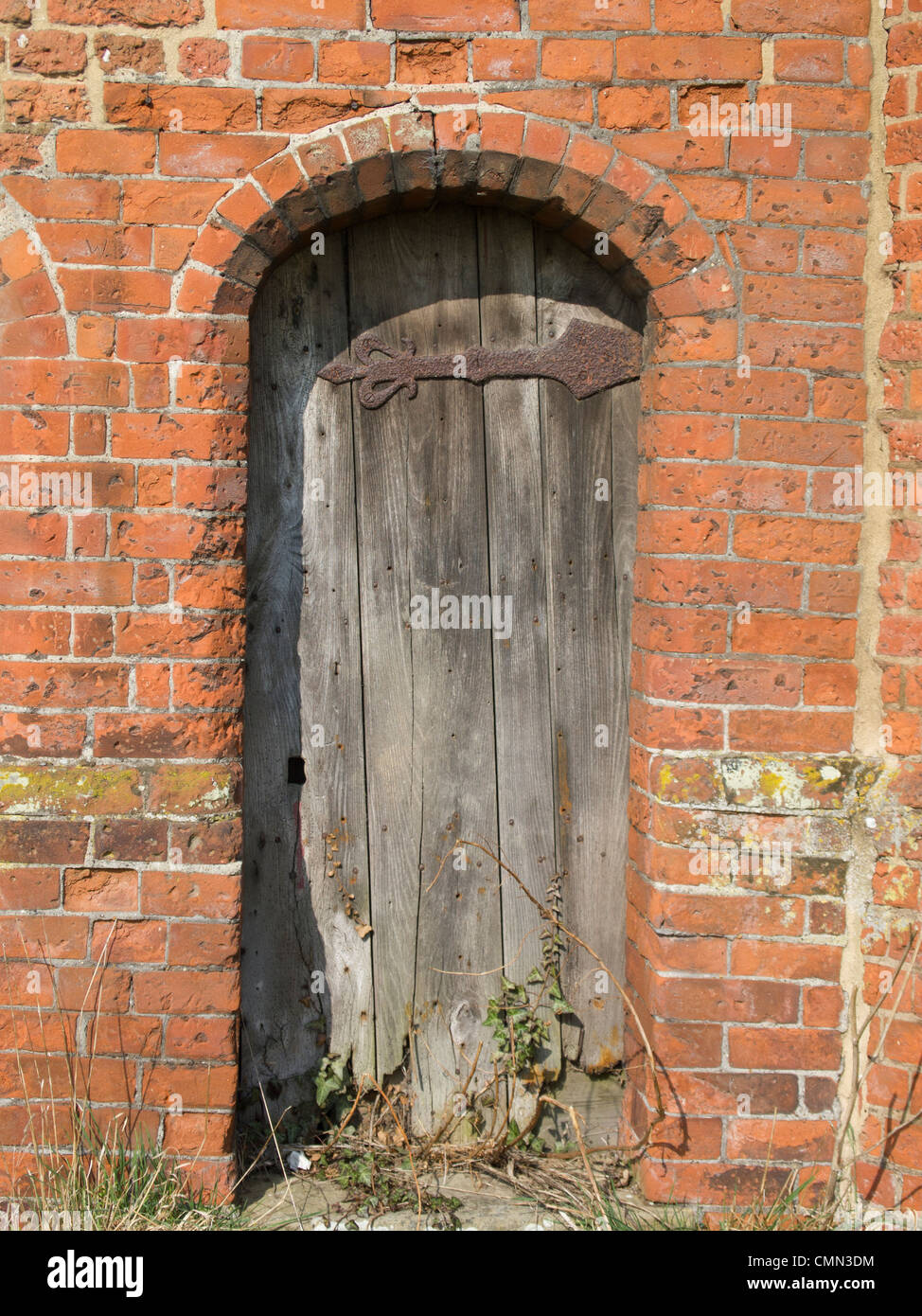 Une vieille porte en bois en décomposition dans une porte voûtée dans un très vieux mur en briques rouges. Banque D'Images