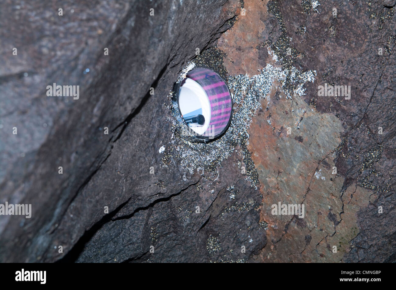 Géocache exposée cachée dans une cavité de paroi rocheuse à l'intérieur d'une grotte volcanique, montrant conteneur et journal de bord. Banque D'Images