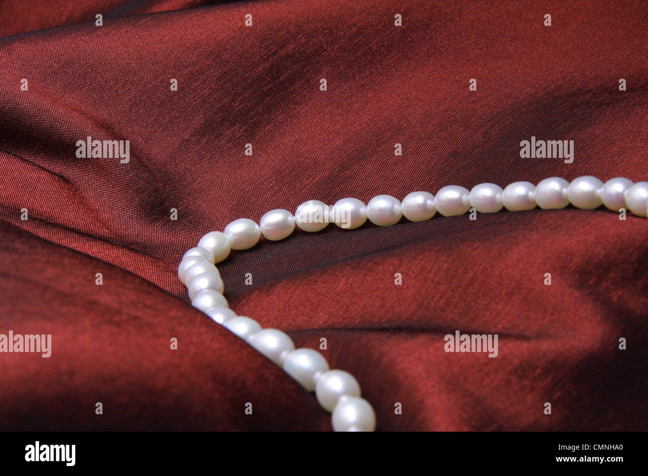 Collier de perles blanches sur satin rouge foncé. Banque D'Images