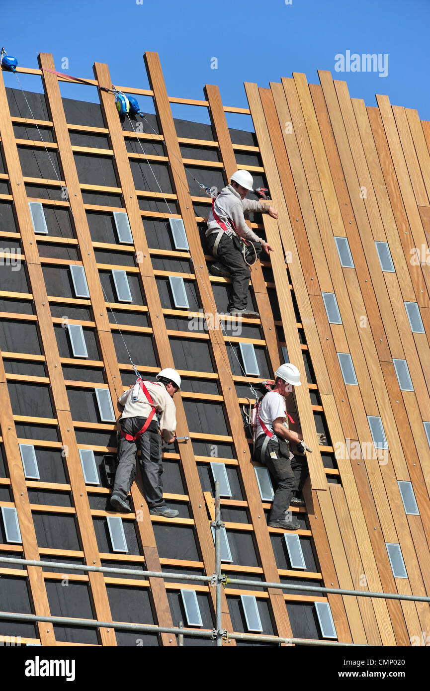 Les travailleurs de la construction / steeplejacks / couvreurs protégés par des harnais de sécurité, casque de sécurité et de cordes de bois de fixation sur toit Banque D'Images