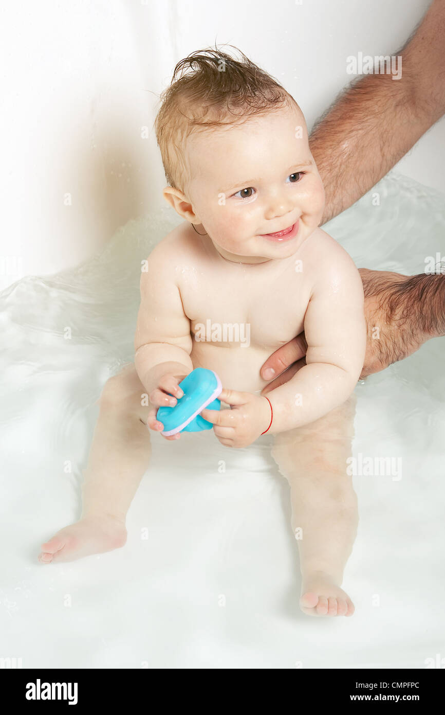 Mignon bébé tenu par les mains du père, jouer avec des jouets en caoutchouc et souriant tout en prenant un bain Banque D'Images