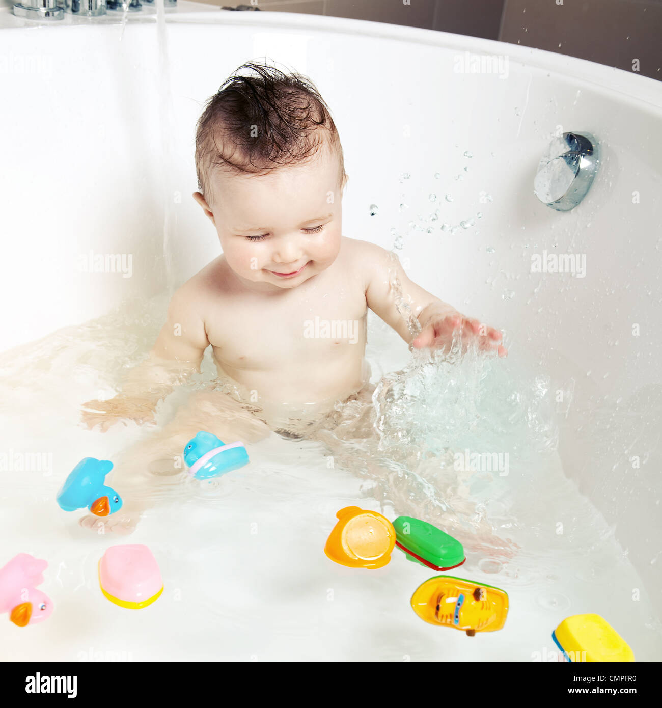 Cute smiling baby s'amusant et aux projections d'eau tout en prenant un bain Banque D'Images