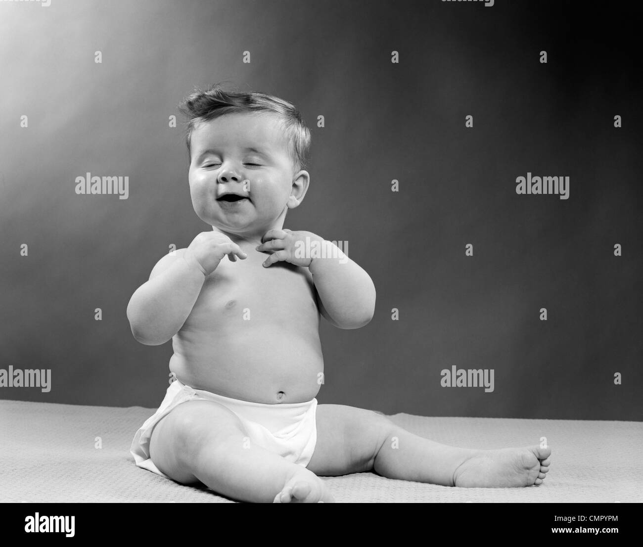 1950 BÉBÉ PORTANT COUCHE ASSIS AVEC LES YEUX FERMÉS POUR OUVRIR LA BOUCHE ET LES MAINS DE TOUCHER LE COU Banque D'Images