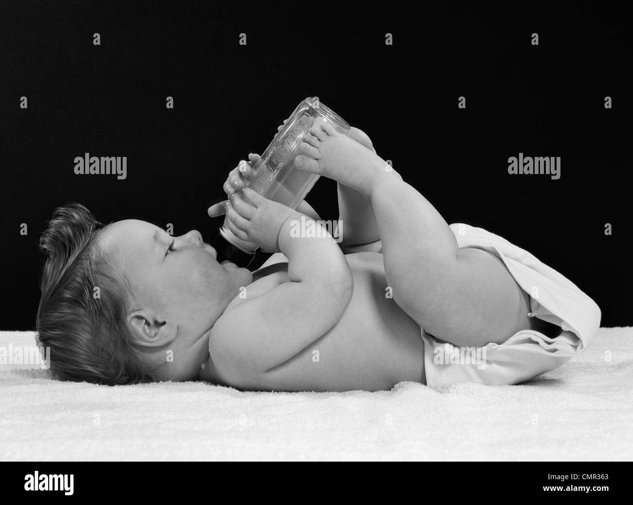 1950 bébé couché sur le dos de la bouteille de boisson tenu par les pieds et mains Banque D'Images