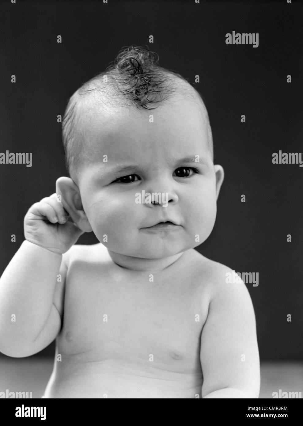 1940 Bebe Avec Legere Les Yeux Plisses Et La Bouche Plissee Tenant La Main Droite Derriere L Oreille Droite Studio Photo Stock Alamy