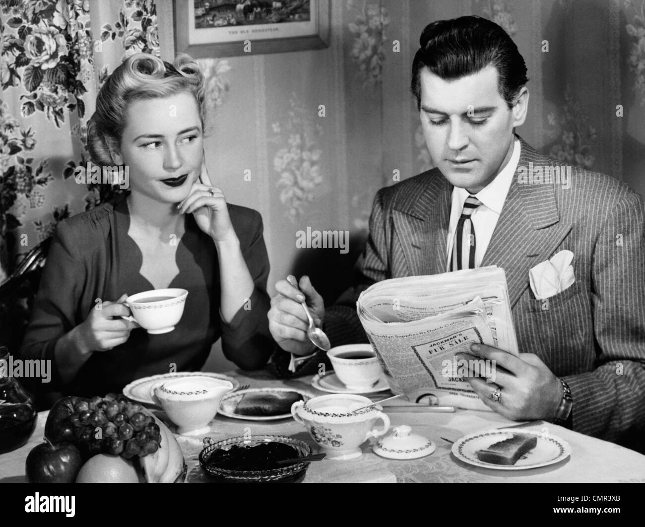 1940 COUPLE TABLE DE PETIT DÉJEUNER IMPATIENT WOMAN MAN READING NEWSPAPER Banque D'Images