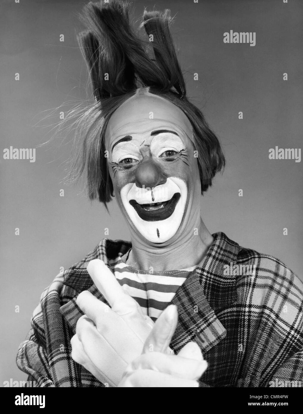 1960 SMILING CLOWN AVEC DES GANTS BLANCS ET MAINS CROISÉES SUR LES CHEVEUX FIN LOOKING AT CAMERA Banque D'Images