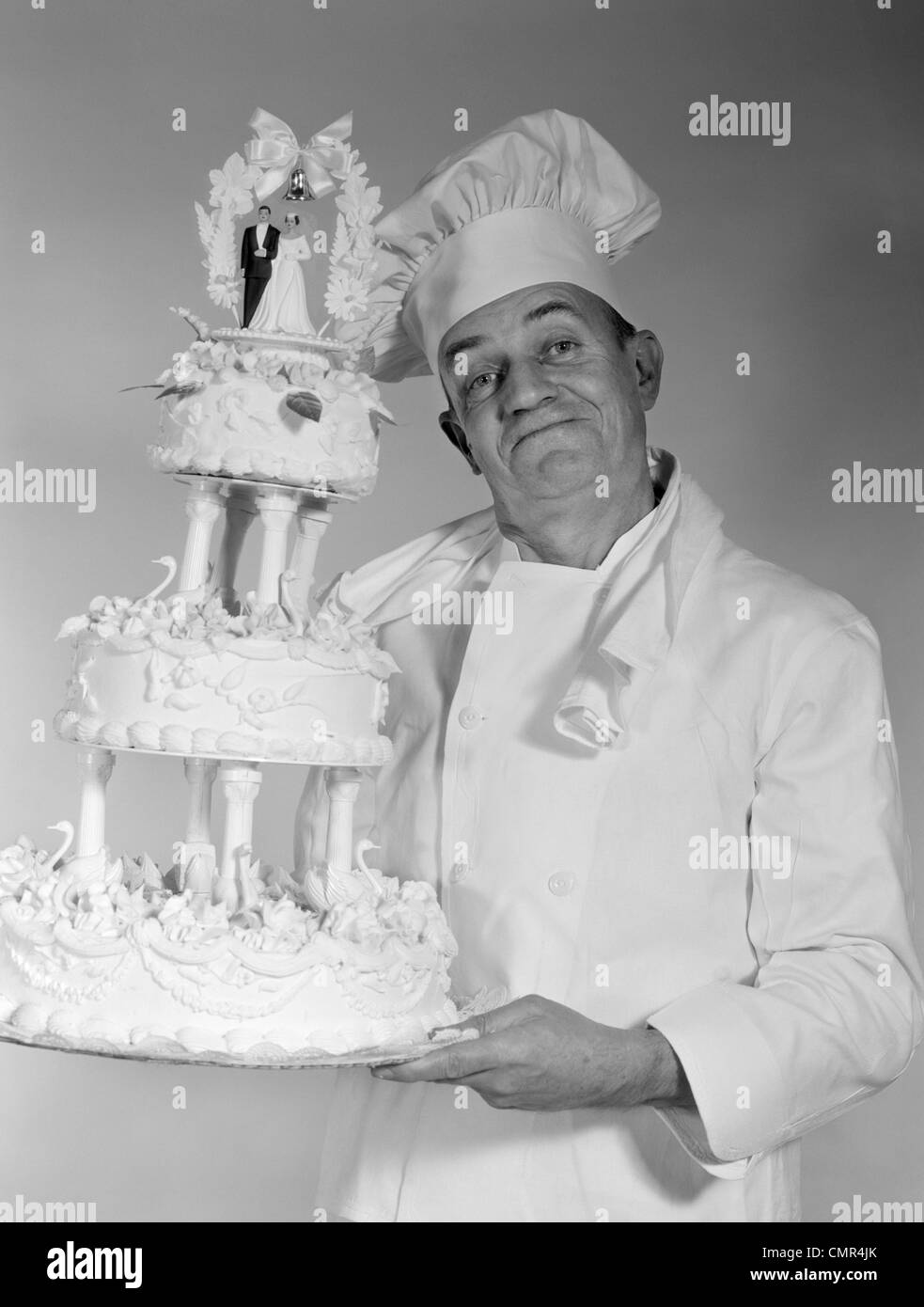 Années 1950 Années 1960 HOMME PLUS ÂGÉ CHEF LOOKING AT CAMERA SMILING HOLDING 3 gâteau de mariage Banque D'Images