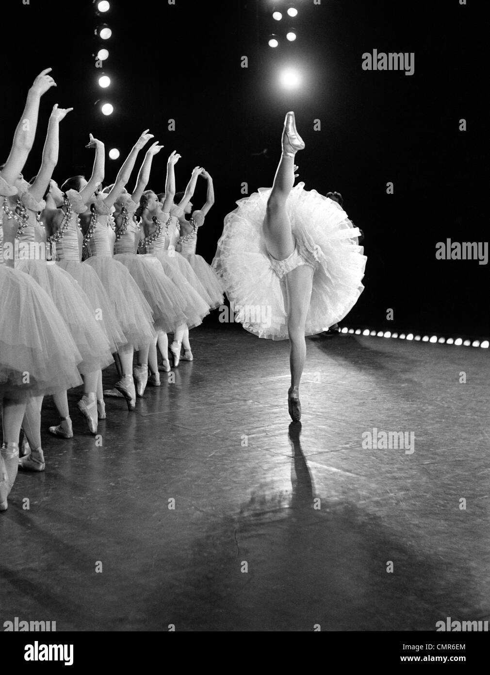 1970 Vue de côté de prima ballerina AU COMITÉ PERMANENT SPLIT avec rangée de 8 danseurs AVEC APPUI BRAS LEVÉS DERRIÈRE ELLE Banque D'Images