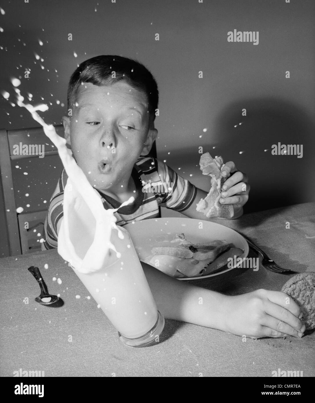 1960 BOY HAVING LUNCH FRAPPER PLUS DE LAIT POUR ATTEINDRE L'INTÉRIEUR SPLASH SURPRISE COOKIE Banque D'Images