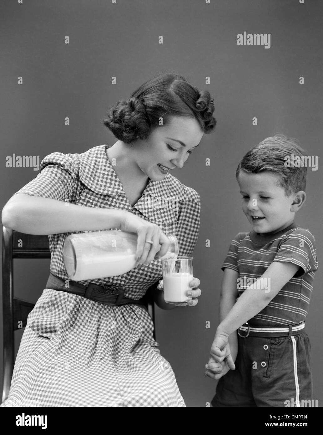 1940 WOMAN MOTHER SITTING POURING VERRE DE LAIT POUR garçon debout à côté de son fils Banque D'Images