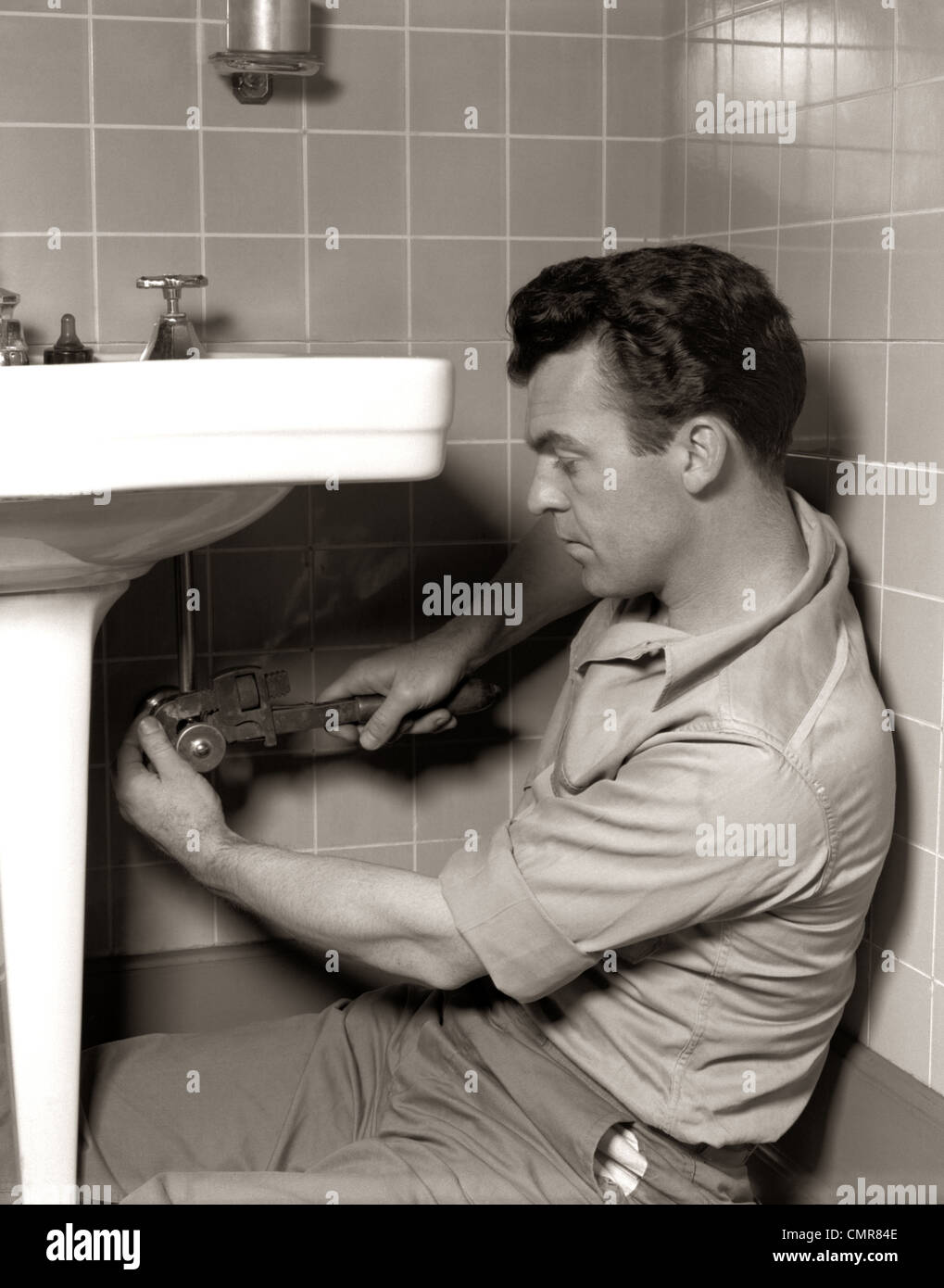 1950 MAN PLUMBER FIXING BATHROOM SINK Banque D'Images