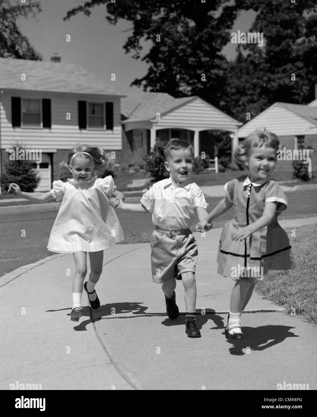 1960 3 ENFANTS SAUTER DE MARCHE EN MARCHE SUR LE TROTTOIR DE BANLIEUE Banque D'Images