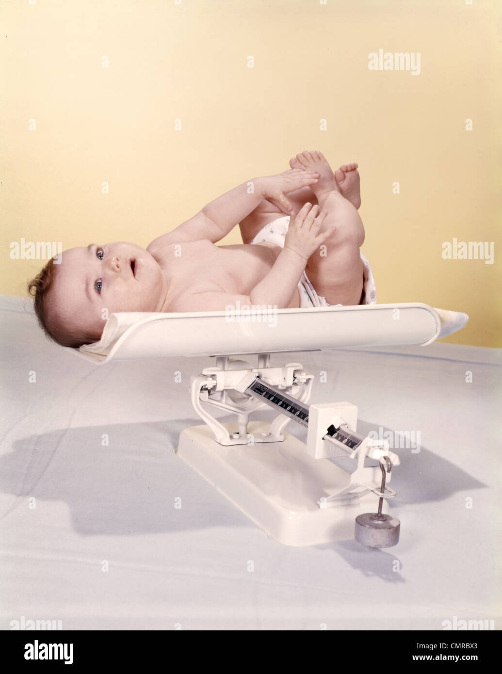 Années 1950 Années 1960 SMILING BABY LYING ON WEIGHT SCALE Banque D'Images