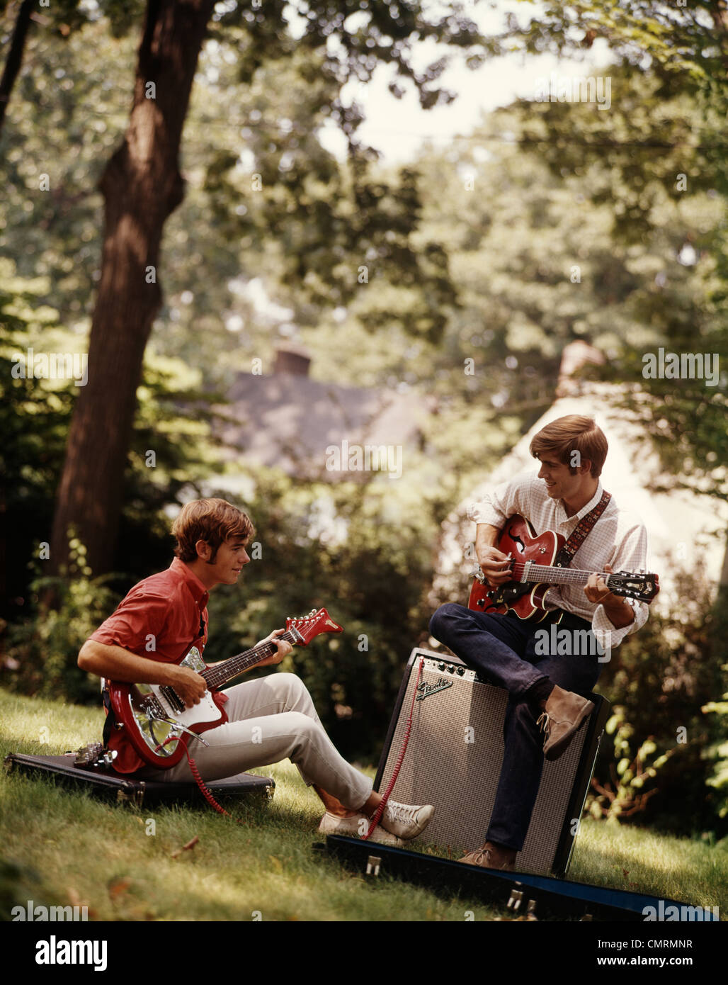 Deux adolescents avec des guitares acoustiques et électriques ASSIS SUR COLLINE AVEC PISCINE ÉQUIPEMENT Banque D'Images