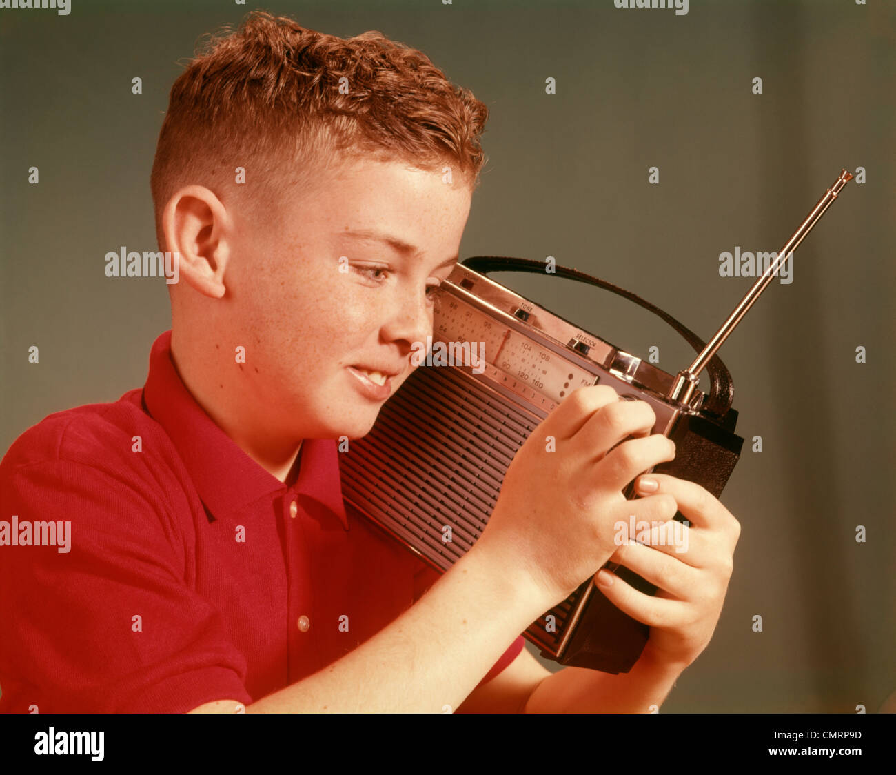 1960 1960 YOUNG PRETEEN BOY LISTENING TO RADIO TRANSISTOR PORTABLE A TENU JUSQU'À L'OREILLE FACE À TRANSISTORS RADIOS RETRO Banque D'Images