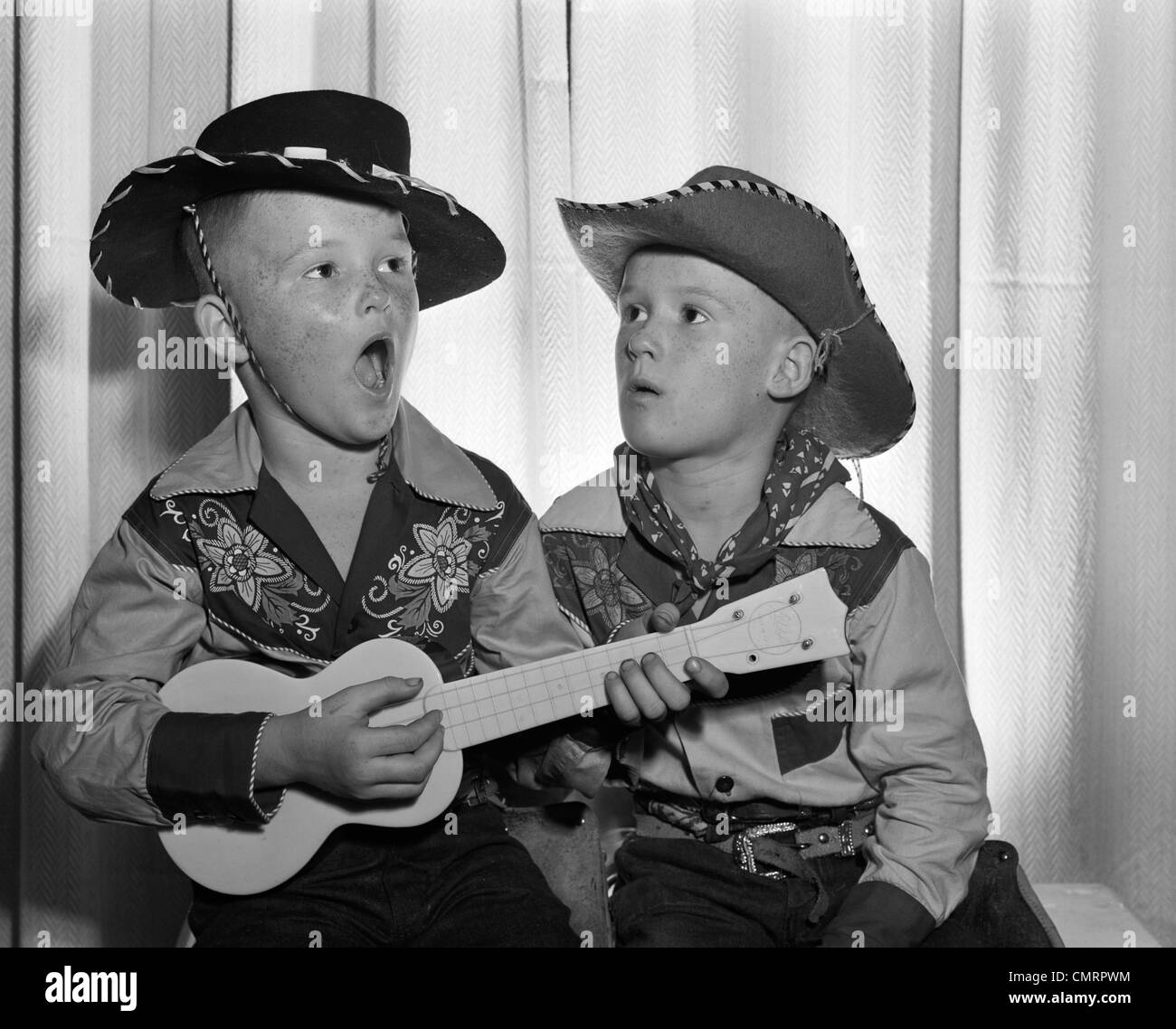 Années 50, 2 jeunes garçons en chapeau de cowboy & SHIRTS JOUER UKULELE & chanter la bouche grande ouverte Banque D'Images