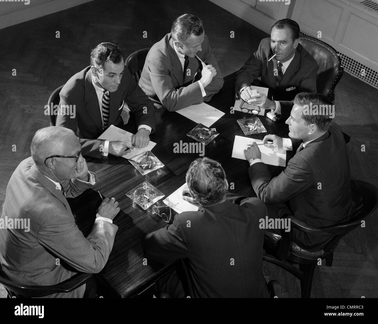 Années 50, GROUPE DE SIX HOMMES PARLER AUTOUR D'UNE TABLE DE CONFÉRENCE Banque D'Images