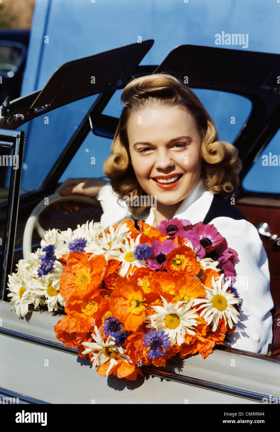 1950 SMILING BLONDE TEEN GIRL SITTING IN CAR DU CONDUCTEUR HOLDING BOUQUET DE FLEURS COLORÉES LOOKING AT CAMERA Banque D'Images