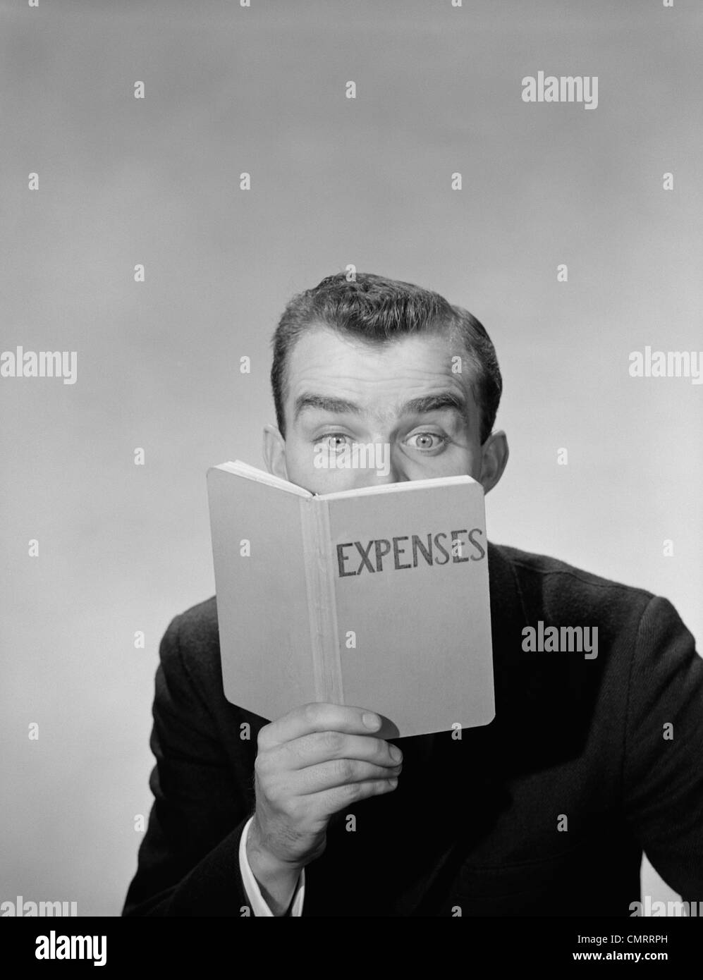 1950 HOMME yeux grands ouverts à la recherche des dépenses en cachant sa face inférieure du livre Banque D'Images