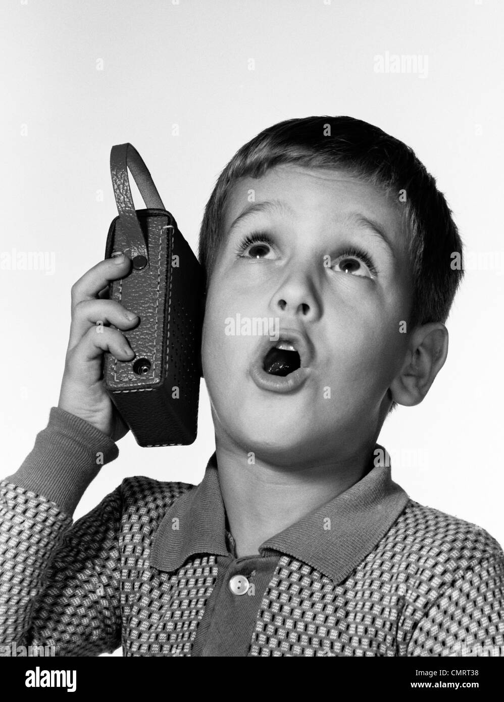 1960 BOY HOLDING RADIO TRANSISTOR JUSQU'À SON OREILLE ALORS QU'IL CHANTE Banque D'Images