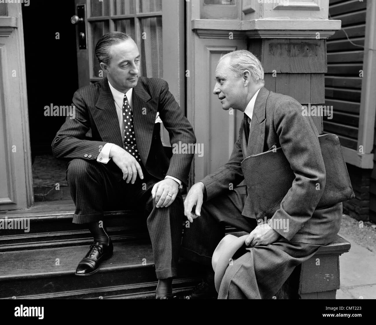 Années 1930 Années 1940 VENDEUR ET PROPRIÉTAIRE DE MAISON HOMME ASSIS ENSEMBLE SUR PRÉSENTATION DE VENTES PARLER AVANT STOOP Banque D'Images