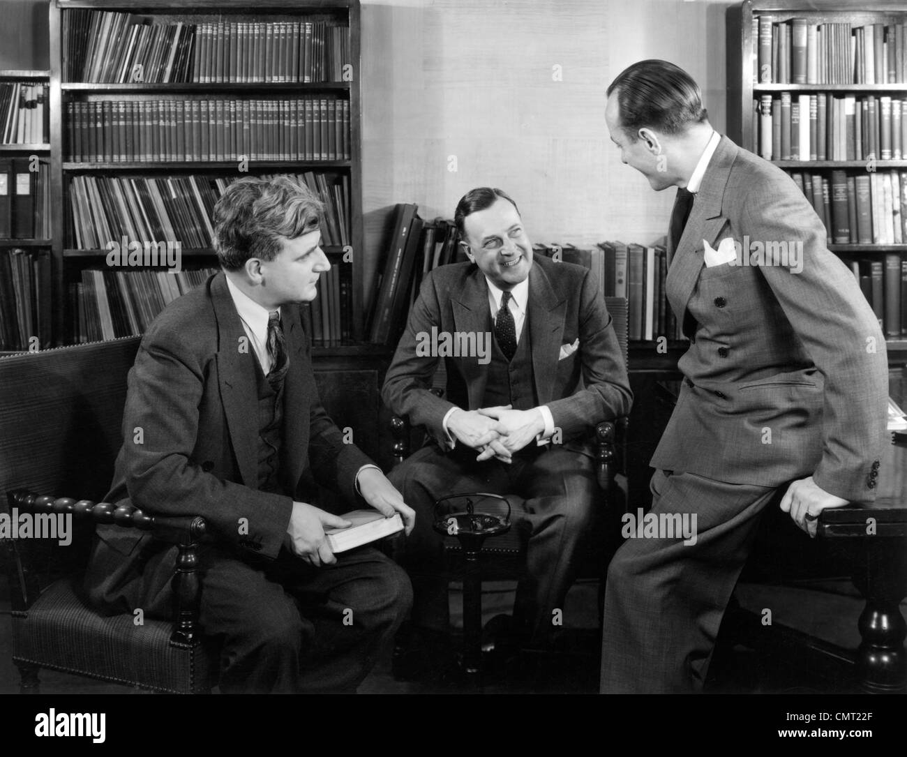 1940 GROUPE DE TROIS HOMMES ASSIS ENSEMBLE EN PARLANT DE BIBLIOTHÈQUE SMILING Banque D'Images