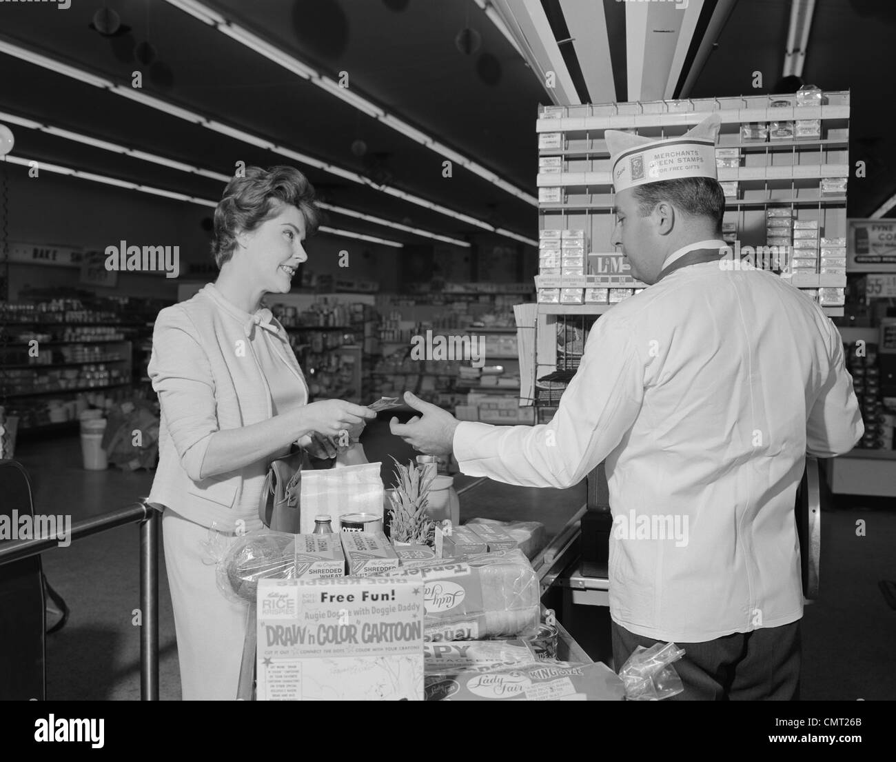 1960 WOMAN PAYING AT GROCERY STORE COMMANDER MALE CASHIER Banque D'Images
